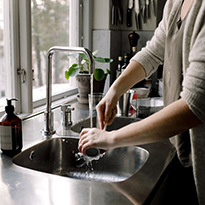 A woman washing dishes at a sink in front of a window.