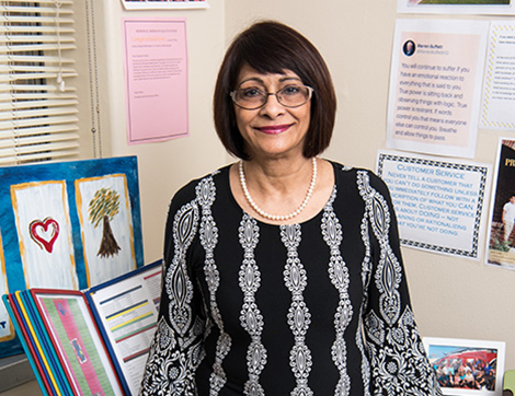 Faizbano Rayani smiles, standing by her work desk adorned with letters and pictures.