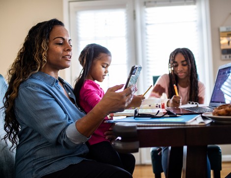 A mother and her two daughters are gathered round the dining table working on different activities.