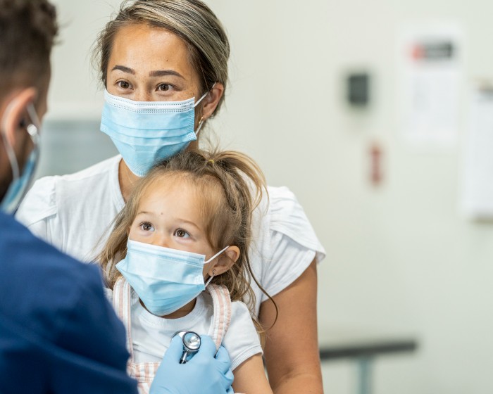 mother and daughter in masks speaking with doctor