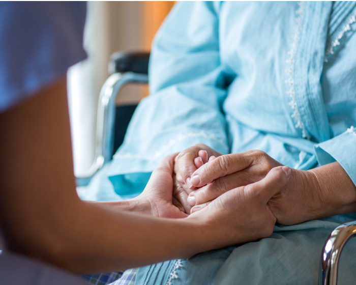 Close-up of a woman in a wheel chair with her hands being held.