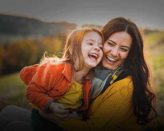 A mother and daughter laugh, as the mother holds and tickles her. 